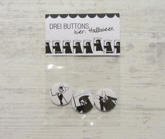 Handgefertigte Halloween-Buttons mit gruseligen Figuren in Schwarz-Weiß. Set aus drei Anstecknadeln mit verschiedenen Motiven: Sensenmann, Geist und Skelett. Verpackung zeigt Reihe stilisierter Sensenmänner. Perfekt für Halloween-Kostüme und gruselige Outfits.