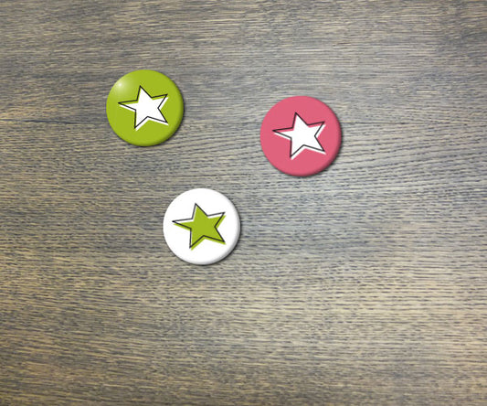 Handgefertigte Buttons mit Sternenmotiv in Grün, Weiß und Pink auf Holzuntergrund. Drei runde Anstecker von Frau Hamster mit individuellen Designs für modische Akzente.