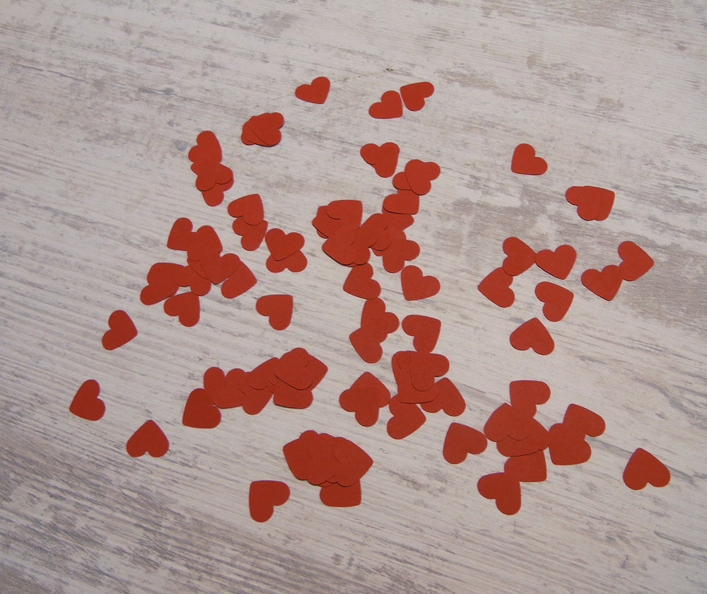 Rote Herzkonfetti aus Papier auf hellem Holzhintergrund. Handgestanzte Herzen in verschiedenen Größen, verstreut für romantische Anlässe wie Hochzeiten oder Valentinstag. Individuelles Dekorationselement von Frau Hamster für festliche Momente.